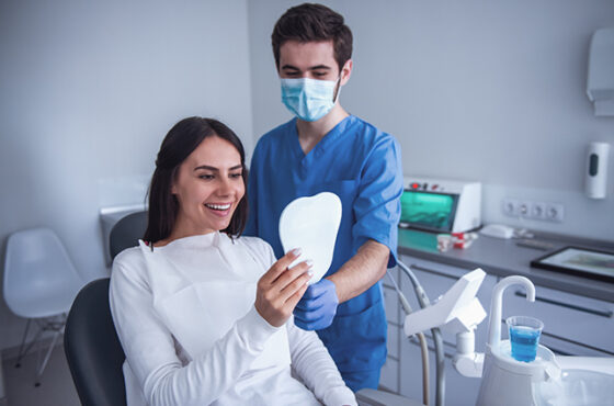 Beautiful young woman is sitting in dentist's chair and smiling, having her teeth treated